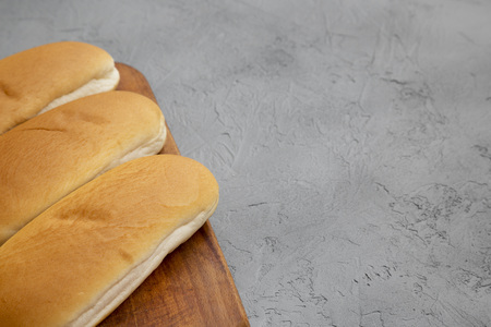 Hot dog buns on rustic wooden board on gray surface, low angle view. Space for text.
