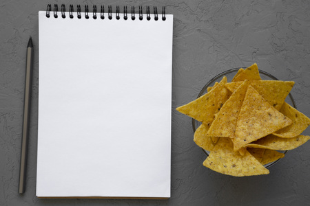 Tortilla chips in glass bowl, blank notepad with pencil over concrete background, top view. Mexican food. From above, overhead.の写真素材