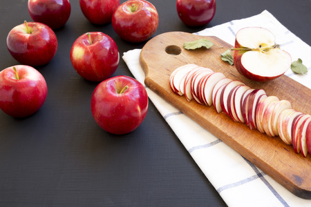 Slices of red apples on rustic wooden board on dark surface, side view.
