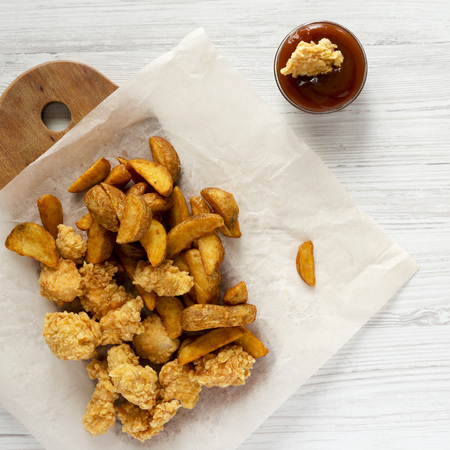 Tasty fast food: fried potato wedges, chicken bites, barbecue sauce, overhead view. Flat lay, top...