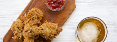 Fried chicken drumsticks with ketchup and cold beer over white wooden background, overhead view.の写真素材