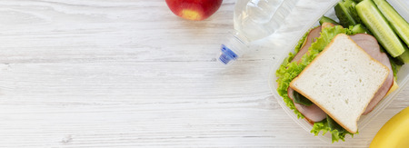 Healthy school lunch box with sandwich, fruits and bottle of water on white wooden surface, top view. From above. Copy space.の写真素材
