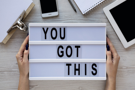 Female hands hold motivation board with text 'You got this'. Feminine workspace. Business concept. Overhead, top view, from above. Flat lay.の写真素材