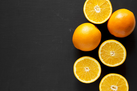 Halved and whole oranges over black background, top view. Overhead, from above, flat lay. Space for text.の写真素材