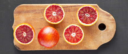Whole and halved blood oranges on rustic wooden board over black background, top view. Flat lay, overhead, from above.の写真素材