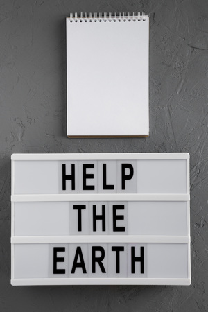 Top view, 'Help the Earth' words on lightbox, blank notepad over gray background, top view. Flat lay, overhead, from above.の写真素材