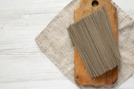 Dried buckwheat soba noodles on rustic wooden board over white wooden background, top view. Copy space.の写真素材