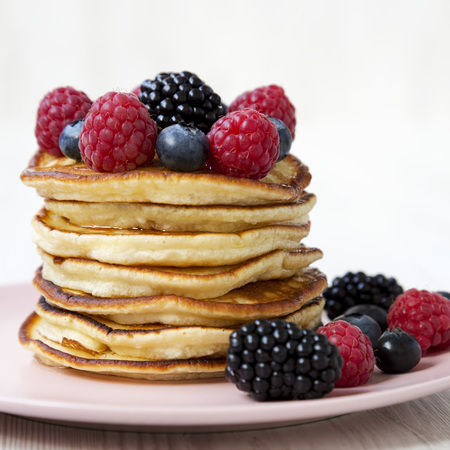 Pancakes with berries on a pink plate on a white wooden surface, side view. Close-up.