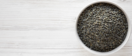 Organic green french lentils in a bowl over white wooden background, top view. Flat lay, overhead, from above. Copy space.の写真素材
