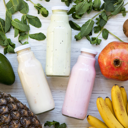Fruit smoothies of different tastes in glass jars with ingredients on white wooden surface. Top view, from above. Flat lay.の写真素材