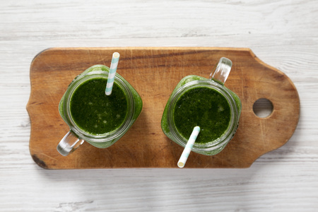 Green smoothie in glass jars on rustic wooden board over white wooden surface, top view. Flat lay, overhead, from above.の写真素材