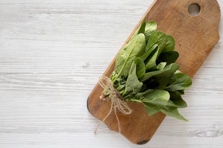 Fresh raw spinach on a rustic wooden board on a white wooden surface. Flat lay, overhead, from...