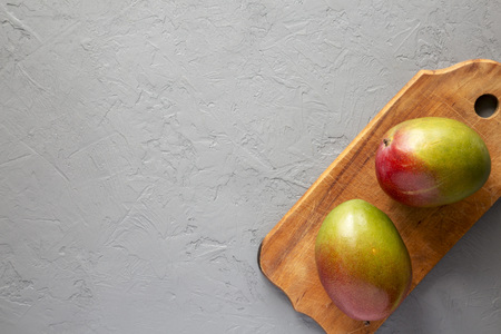 Fresh sweet mangoes on rustic wooden board on concrete background, top view. Flat lay, from above, overhead. Copy space.の写真素材