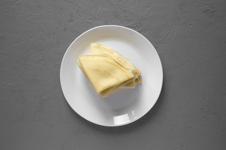 Pile of tasty blini on a white plate over gray background, top view. Flat lay, overhead, from above. Close-up.の写真素材