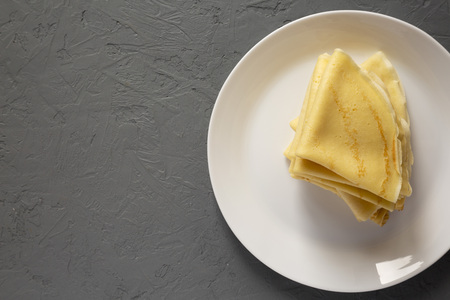 Pile of tasty blini on a white plate over concrete background. Flat lay, overhead, from above. Copy space.の写真素材