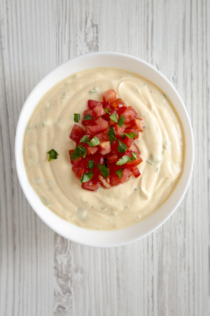 Overhead view, homemade cheesy dip in a bowl over white wooden background. From above, flat lay, top...