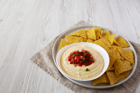 Homemade cheesy dip in a bowl, yellow tortilla chips, side view. Space for text.