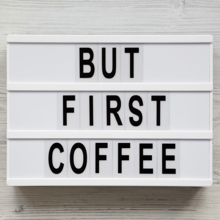 'But first coffee' words on modern board over white wooden surface, top view. Overhead, flat lay,...