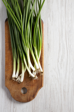 Fresh green onions on a cutting board on a white wooden table, top view. From above, overhead, flat lay. Copy space.の写真素材