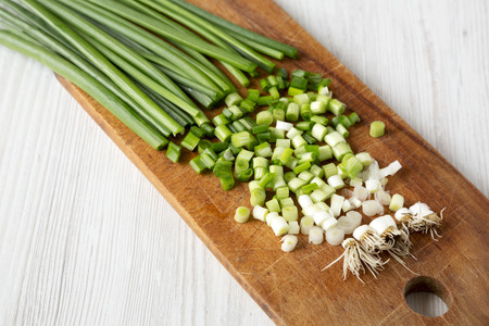 Chopped green onions on a rustic wooden board over white wooden background, side view. Close-up.