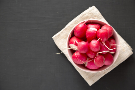 Fresh red radishes in a pink bowl over black surface, top view. Flat lay, from above, overhead. Copy space.の写真素材
