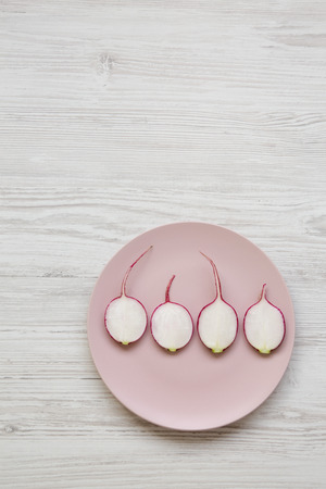 Radish slices on a pink plate over white wooden surface, top view. Overhead, from above, flat lay. Copy space.の写真素材