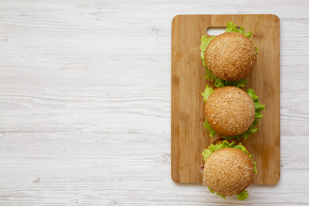 Homemade cheeseburgers on a bamboo board over white wooden background, overhead view. Flat lay, from above, top view. Copy space.の写真素材