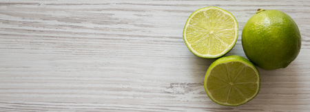 Whole and cut green citrus limes on a white wooden surface, top view. Overhead, from above. Copy space.の写真素材