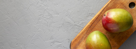 Fresh sweet mangoes on a rustic wooden board over gray background, top view. Flat lay, from above, overhead. Copy space.の写真素材