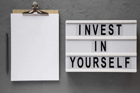 'Invest in yourself' words on a modern board, clipboard with blank sheet of paper over concrete background, top view. Overhead, flat lay, from above.の写真素材