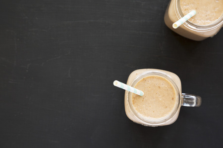 Healthy banana apple smoothie in glass jars over black background, top view. Flat lay, from above, overhead. Copy space.の写真素材