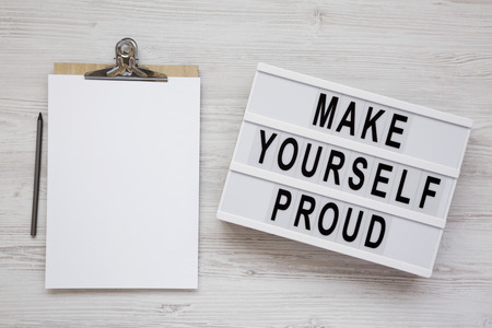 Lightbox with 'Make yourself proud' words, clipboard with blank sheet of paper on a white wooden background, top view. Flat lay, overhead, from above.の写真素材