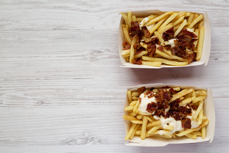 French fries with cheese sauce and bacon in paper boxes over white wooden surface, top view. Flat lay, from above, top view. Copy space.の写真素材