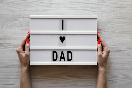 Female hands hold lightbox with 'I love dad' words over white wooden surface, top view. Overhead, from above, flat lay. の写真素材