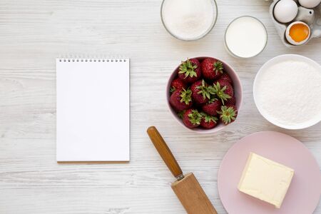 Strawberry pie ingredients (flour, eggs, butter, milk, sugar, strawberry) and blank notepad, top view. Cooking strawberry pie or cake. Flat lay, overhead, from above.の写真素材