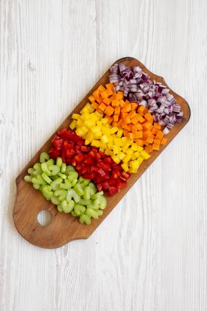 From above, chopped fresh vegetables (carrot, celery, red onion, colored peppers) arranged on a cutting board on a white wooden surface. Flat lay, from above, top view. Close-up.の写真素材