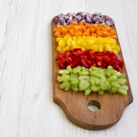Chopped fresh vegetables (carrot, celery, red onion, peppers) arranged on a cutting board on a white wooden background, low angle view. Copy space.の写真素材