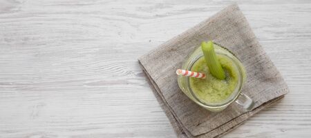 Glass jar of green celery smoothie on a white wooden background, top view. Flat lay, from above, overhead. Space for text.の写真素材