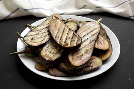 Grilled eggplant on a white plate on a black background, side view. Close-up.の写真素材