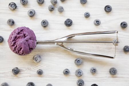 Blueberry ice cream sorbet in ice cream scoop on a white wooden background, top view. Overhead, from...