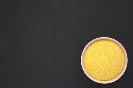 Dry organic Masarepa corn meal in a pink bowl over black background, top view. Flat lay, overhead, from above. Copy space.の写真素材
