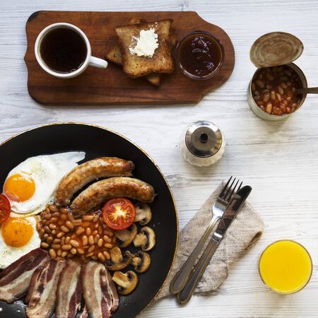 Full English breakfast in a pan with fried eggs, bacon, beans, sausages  and toasts on white wooden surface, top view. Close-up. Flat lay. From above, overhead.の写真素材