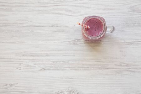 Glass jar with smoothie made of banana, black currant, coconut milk on a white wooden table, top view. Overhead, from above. Copy space.の写真素材
