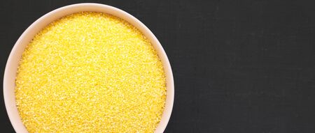 Dry organic Masarepa corn meal in a pink bowl over black background, top view. Flat lay, overhead, from above. Space for text.の写真素材