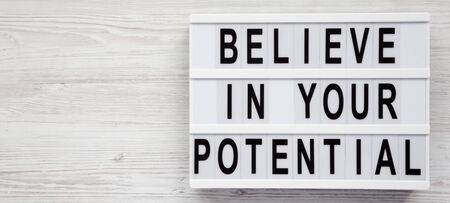 'Believe in your potential' words on a lightbox on a white wooden surface, top view. Space for text.の写真素材