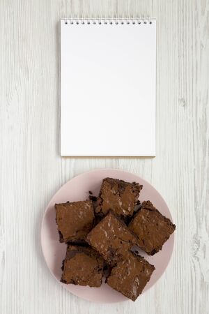 Homemade chocolate brownies on a pink plate, blank notepad, top view. Flat lay, overhead, from above. Copy space.の写真素材