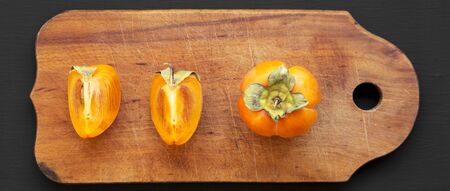 Fresh persimmon on a rustic wooden board on a black background, top view. Flat lay, overhead, from above. Close-up.の写真素材