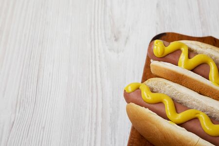 Hotdog with yellow mustard on a rustic wooden board on a white wooden background, low angle view. Copy space.の写真素材
