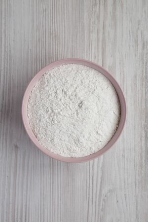 Gluten free rice flour in a pink bowl over white wooden background,  top view. Flat lay, overhead, from above.の写真素材