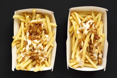 French fries with cheese sauce and onion in paper boxes on a black background, overhead view. Flat...